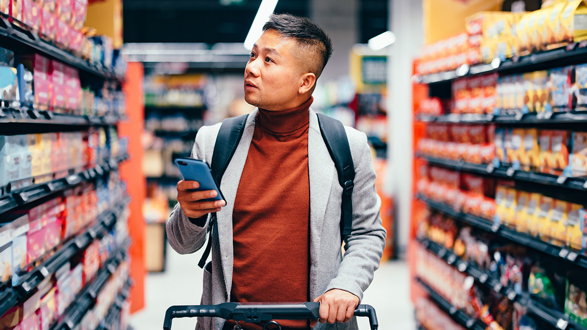 Handsome Asian Male Searching For Groceries From The List On His Mobile Phone